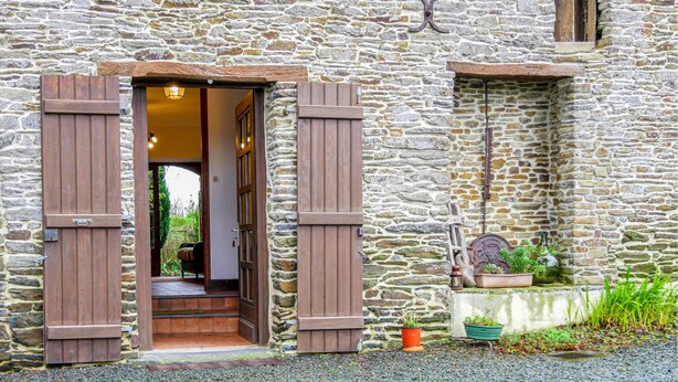 Un bâtiment en pierre avec des volets en bois, une petite fenêtre et un pot de fleurs posé sur le sol.