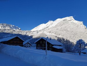 Una montaña cubierta de nieve bajo un cielo azul despejado. Se observan cabañas de madera con nieve en los tejados.