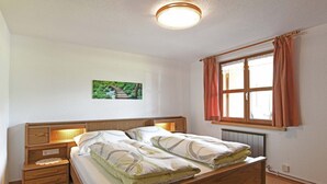 Ein Schlafzimmer mit einem hölzernen Bett, Nachttischen, einer Heizung und einem Fenster mit Vorhängen.