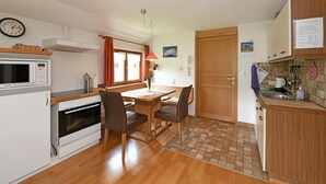 Eine kompakte Küche mit Mikrowelle, Backofen und Spüle, ein Essbereich mit Stühlen sowie eine Holztür.