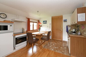 Cocina compacta con microondas, horno y lavamanos, zona de comedor con sillas, y una puerta de madera.