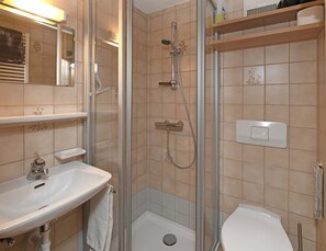 Un baño con ducha envuelta en cristal, un lavamanos y un inodoro.