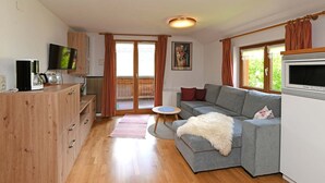 A living room with a grey sofa, wooden cabinet, flat-screen TV, and a dining area with a table and chairs. - Holiday apartment Üntschenspitze - Gästehaus Margreth (Au)