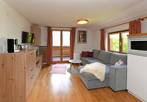A living room with a grey sofa, wooden cabinet, flat-screen TV, and a dining area with a table and chairs. - Holiday apartment Üntschenspitze - Gästehaus Margreth (Au)