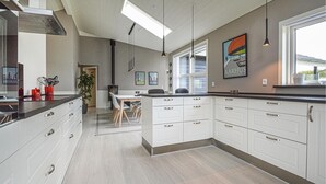 Une cuisine moderne avec des meubles blancs, un îlot central, des luminaires suspendus et une grande fenêtre qui laisse entrer la lumière naturelle.