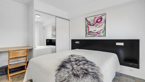 Een moderne slaapkamer met een groot bed, een houten stoel, een bureau en twee abstracte schilderijen aan de wanden.