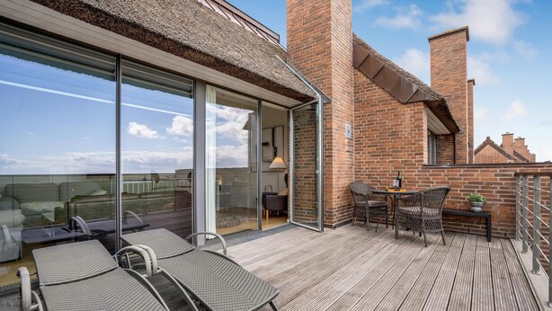 Een balkon met rieten stoelen, een tafel en een plant in pot.