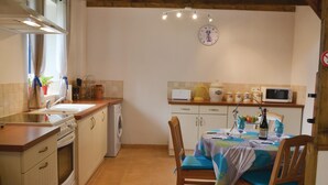 Cocina compacta con lavamanos, estufa y microondas. Hay una mesa de comedor con sillas y un reloj en la pared.