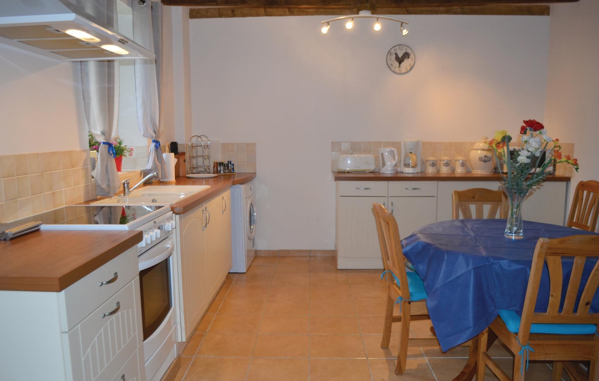 Una cocina con lavaplatos, estufa y lavavajillas. Hay una mesa de comedor con sillas y un jarrón de flores.