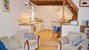 Una sala acogedora con dos sofás y una mesa de comedor, una cocina con electrodomésticos básicos y una escalera que conduce a un nivel superior.
