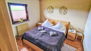 A neatly made bed with a dark patterned bedspread, two white pillows, and a small bedside table with a lamp.