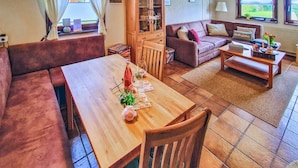 A cozy living room with a wooden dining table, cushioned seating, and a sofa.