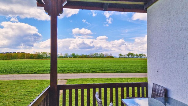 A covered outdoor area with a view of a green field and trees in the distance.