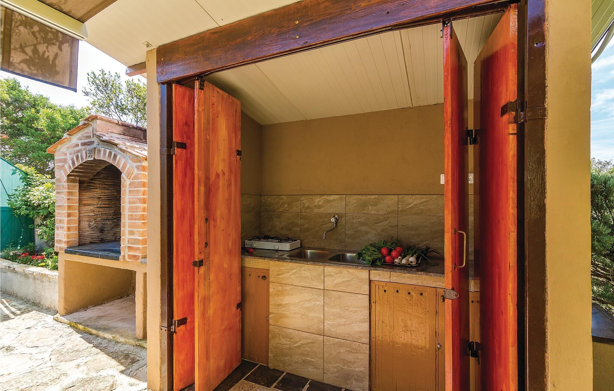Cocina compacta con horno de ladrillo, un lavabo y una encimera con verduras.
