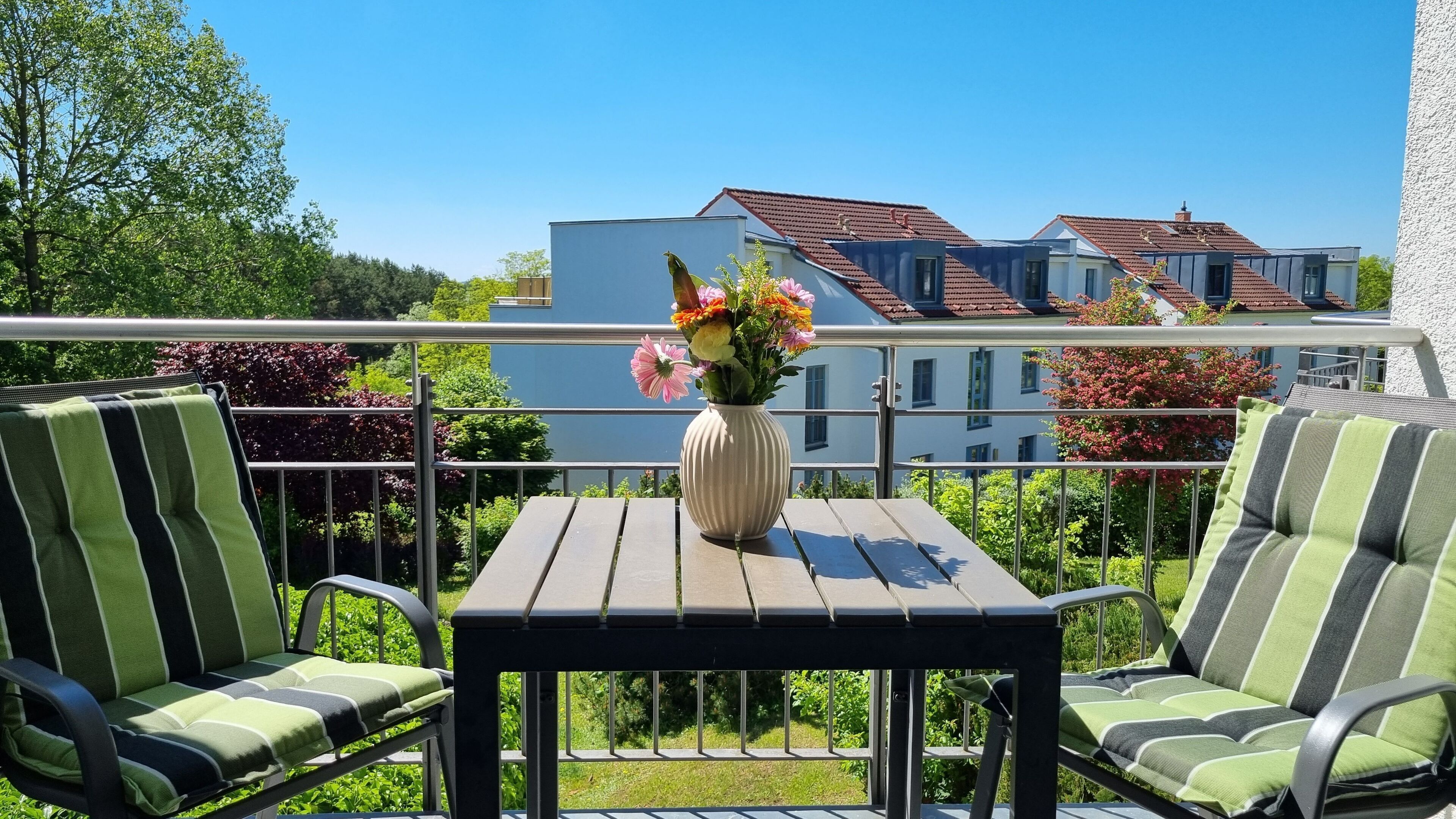 Ein Balkon mit zwei gestreiften Stühlen, einem kleinen Tisch und einem Blumenstrauß.