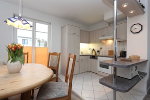 A modern kitchen with white cabinets, a built-in oven, and a dining area with a wooden table and chairs.