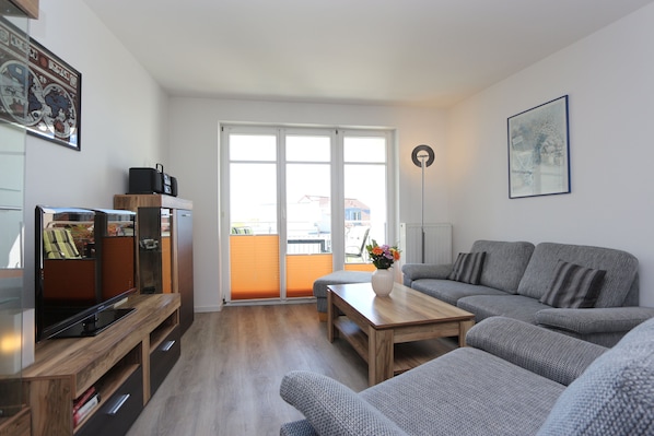 A modern living room with a grey sofa, wooden coffee table, and a flat-screen TV on a wooden stand.