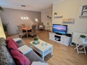Un salon comprenant un canapé, une table basse, un téléviseur et un coin repas avec des chaises et une table.