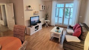 A modern living room with a flat-screen TV, a dining table, and a sofa. - (224) 2-room apartment - apartment house Strandburg (Kühlungsborn)
