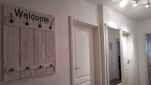 A hallway with a wooden wall-mounted sign reading "Welcome," a white door, and a mirror. - (224) 2-room apartment - apartment house Strandburg (Kühlungsborn)