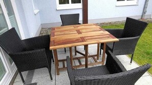 A square wooden table with a woven chair design, surrounded by four chairs, set on a patio with a house in the background. - (224) 2-room apartment - apartment house Strandburg (Kühlungsborn)