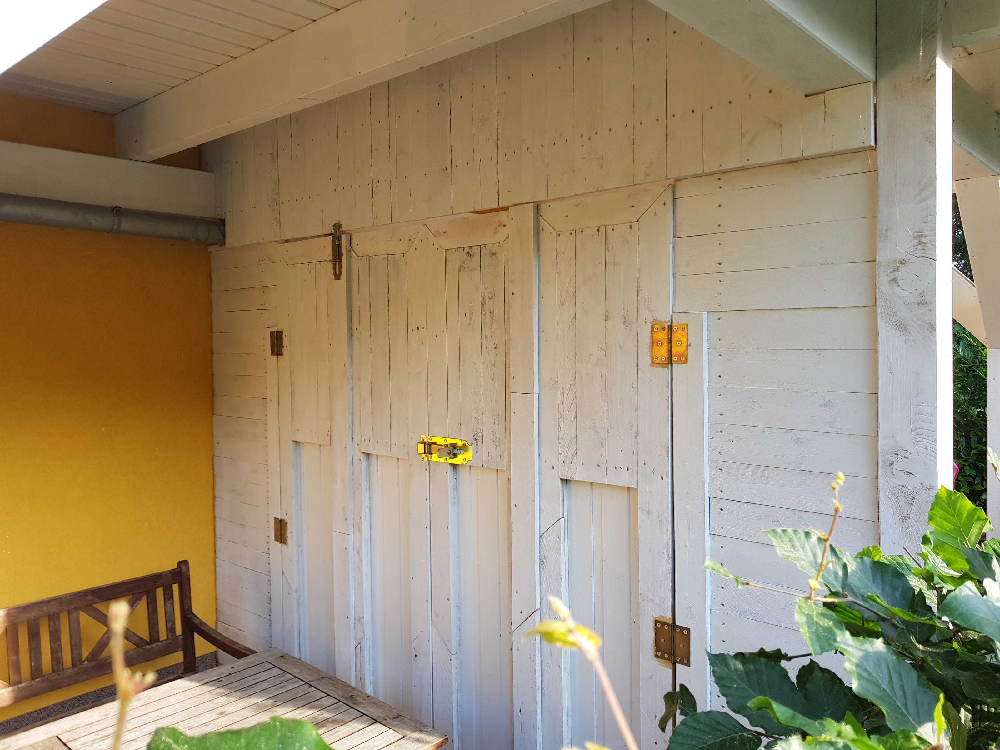 Une pièce en bois avec un banc, une porte dotée d’un cadenas jaune et une plante.