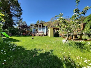 En rymlig trädgård med en träaltan, en liten lekplats och en lusthus.