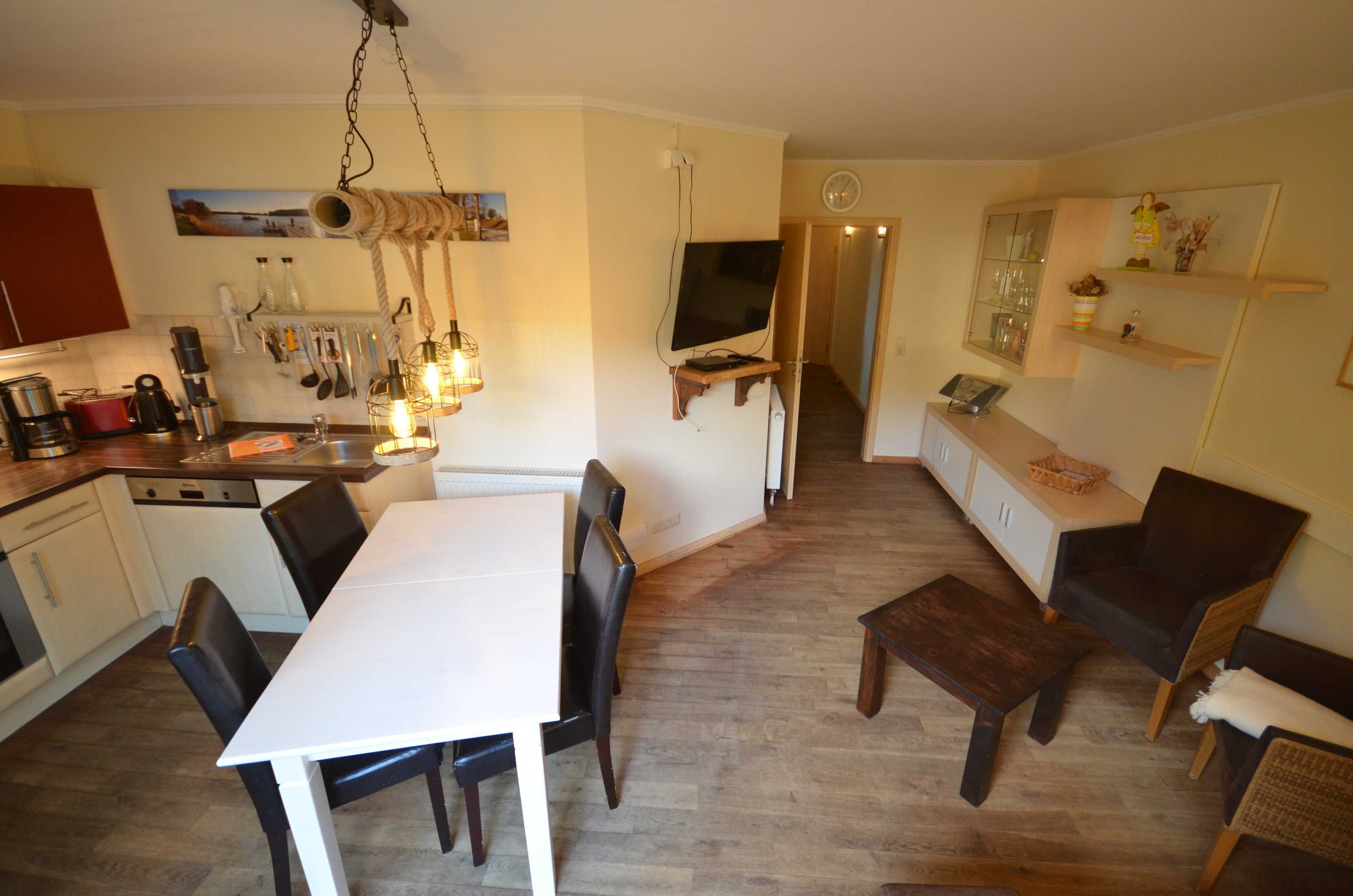 Une cuisine compacte avec un coin repas, un plancher en bois et un téléviseur fixé au mur.