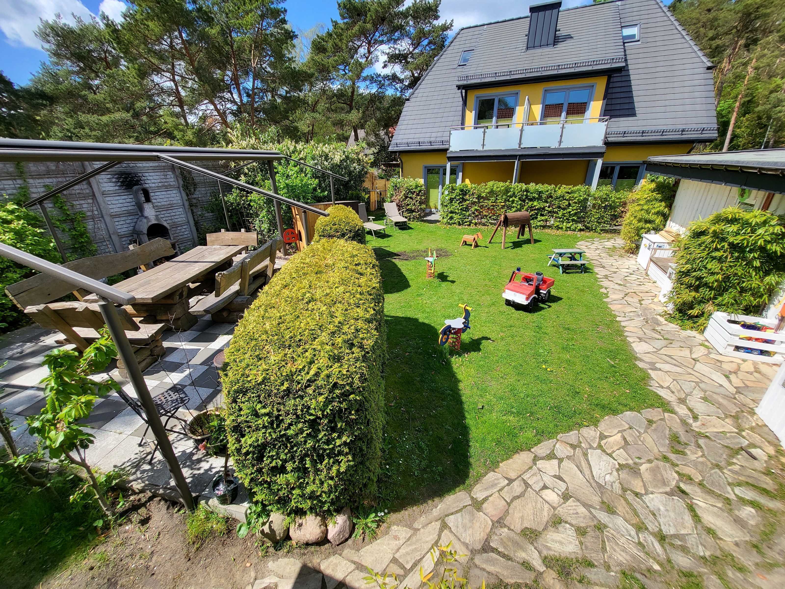 A well-maintained backyard with a stone pathway, a wooden play structure, and a yellow house with a grey roof.