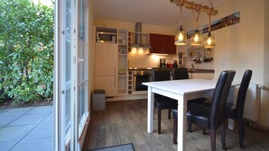 Et lille køkken med hvide skabe, et spisebord med stole og en hængende lampe.