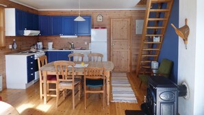 Una cocina compacta con armarios de madera, una mesa de comedor con sillas, una estufa y una escalera de madera.
