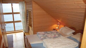 Un dormitorio de cabaña de madera con una cama, una mesita de noche con lámpara y una ventana con cortinas.