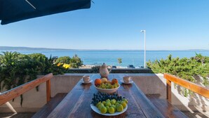 Una mesa con frutas y vasos en una terraza con vistas al mar.