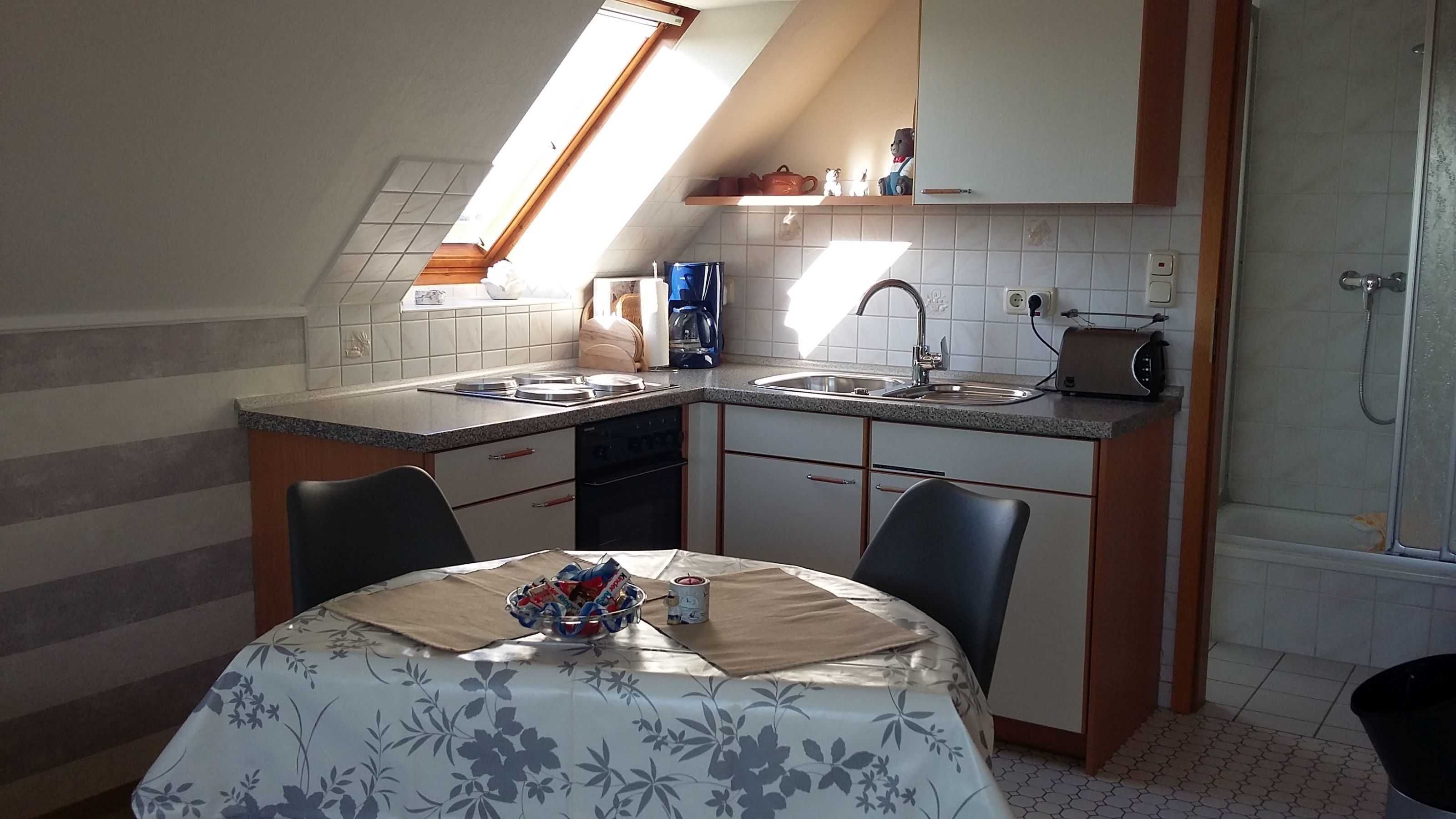A compact kitchen with a built-in oven, a sink, and a toaster. There is a dining table with a floral tablecloth and chairs.