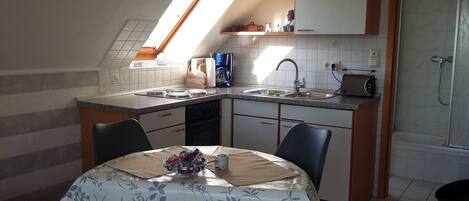 A compact kitchen with a built-in oven, a sink, and a toaster. There is a dining table with a floral tablecloth and chairs.
