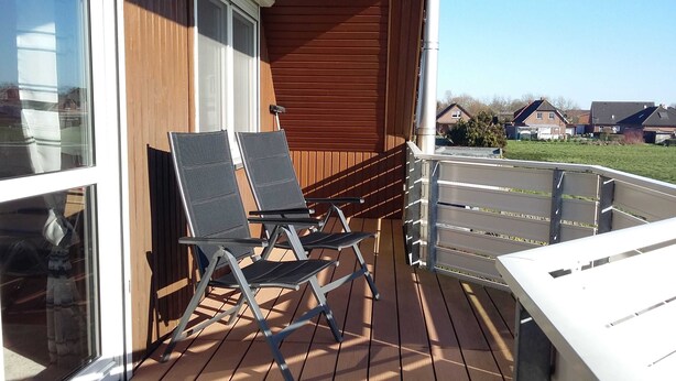 A wooden deck with two lounge chairs and a white table.