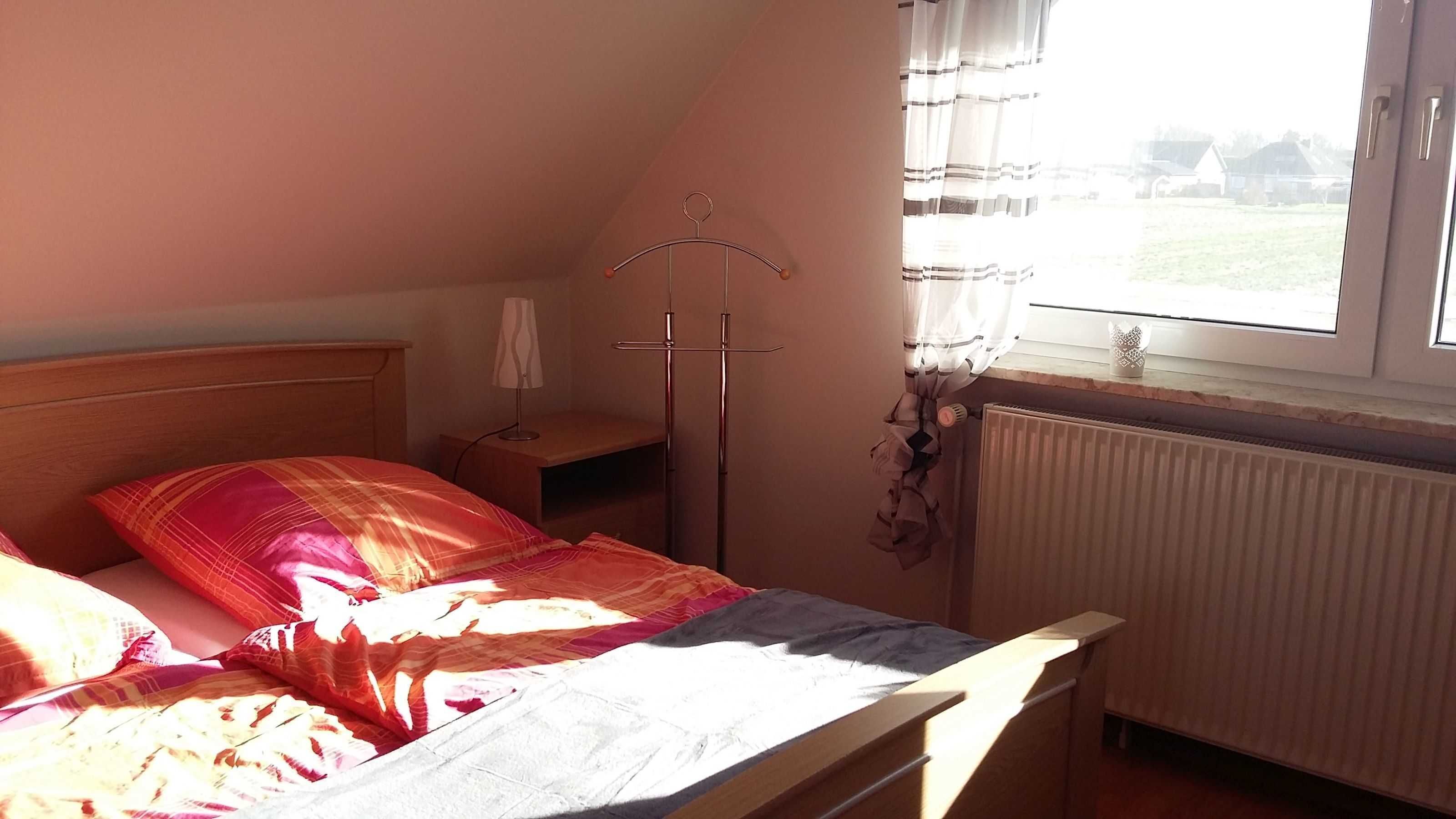 Een slaapkamer met een bed, nachtkastje, lamp, radiator en een raam met gordijnen.