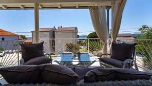 A covered outdoor seating area with wicker furniture and cushions, overlooking a residential area with houses and a clear sky. - Stunning home in Sv.Filip i Jakov (Sv.Filip i Jakov)