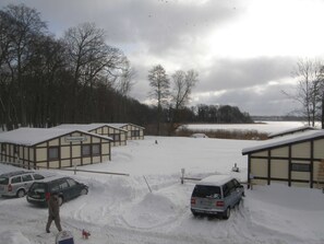 Una hilera de cabañas sobre un terreno cubierto de nieve, una masa de agua al fondo y un cielo nublado.