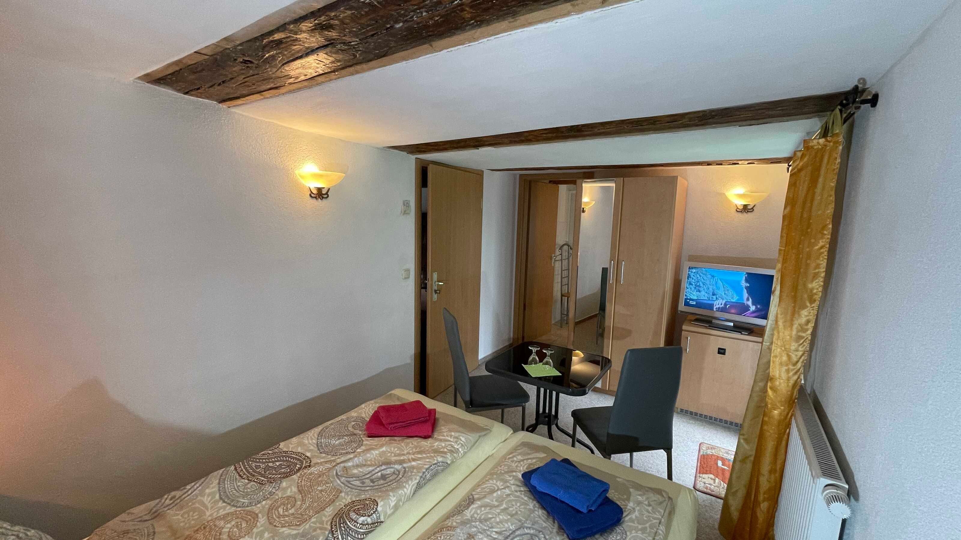 Une chambre d’hôtel avec un lit, un bureau, une chaise, une télévision et une salle de bain visible à travers une porte ouverte.