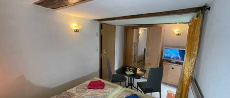 Une chambre d’hôtel avec un lit, un bureau, une chaise, une télévision et une salle de bain visible à travers une porte ouverte.