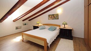Une chambre avec un lit en bois, deux tables de chevet avec des lampes, un tapis blanc et un plafond en pente avec des poutres apparentes.