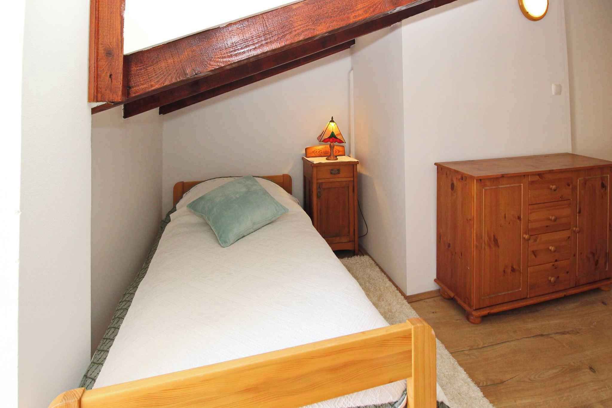 A small bedroom with a single bed, a nightstand with a lamp, and a wooden dresser.