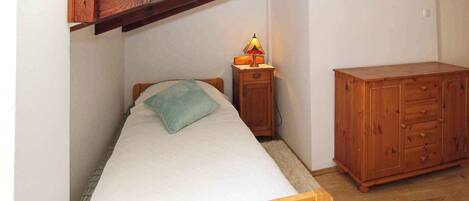 A small bedroom with a single bed, a nightstand with a lamp, and a wooden dresser.