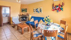 Una sala de estar acogedora con chimenea, un sofá, una mesa de comedor con sillas y una zona de cocina con ventana.