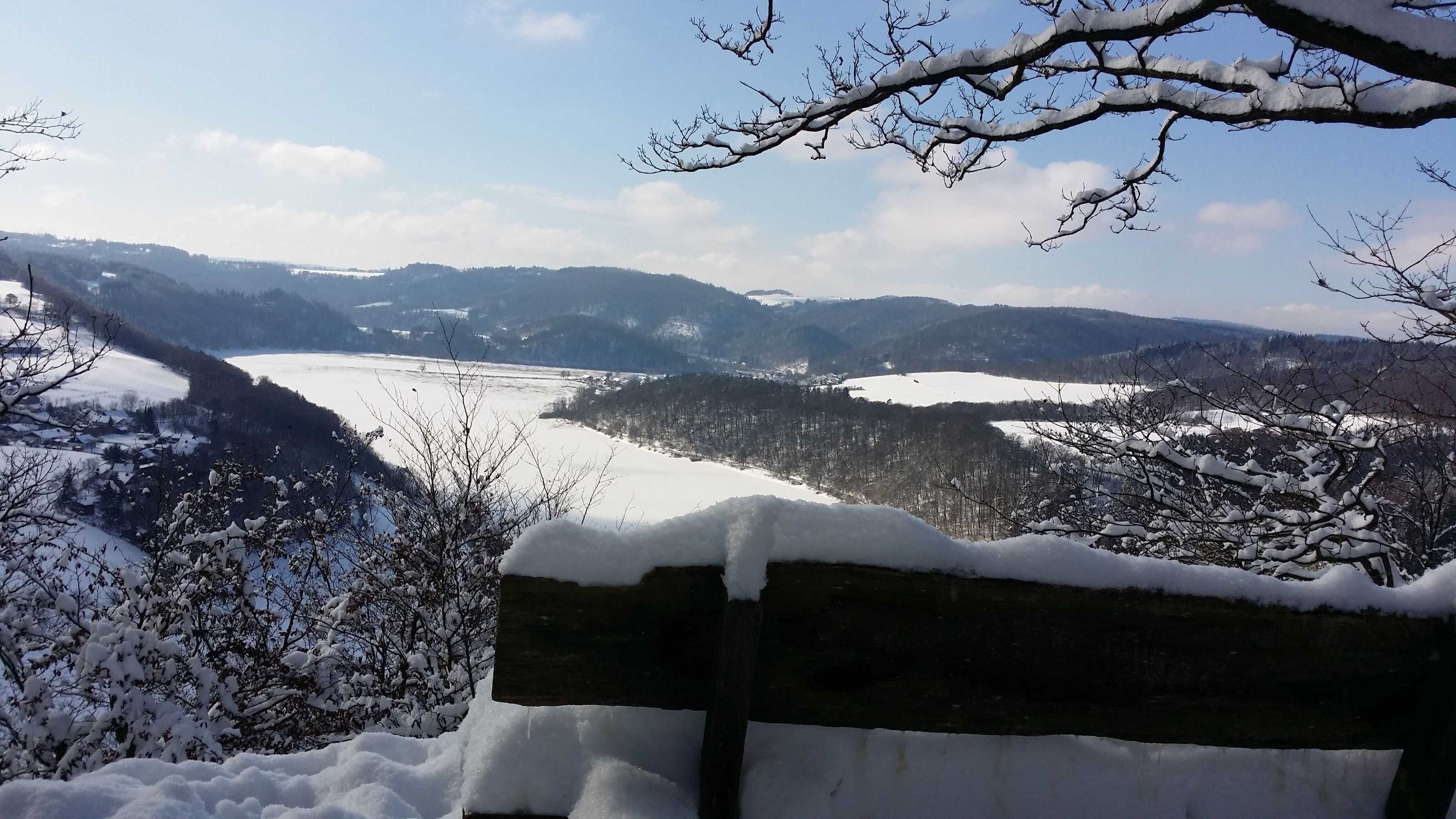A snowy landscape with a bench in the foreground.