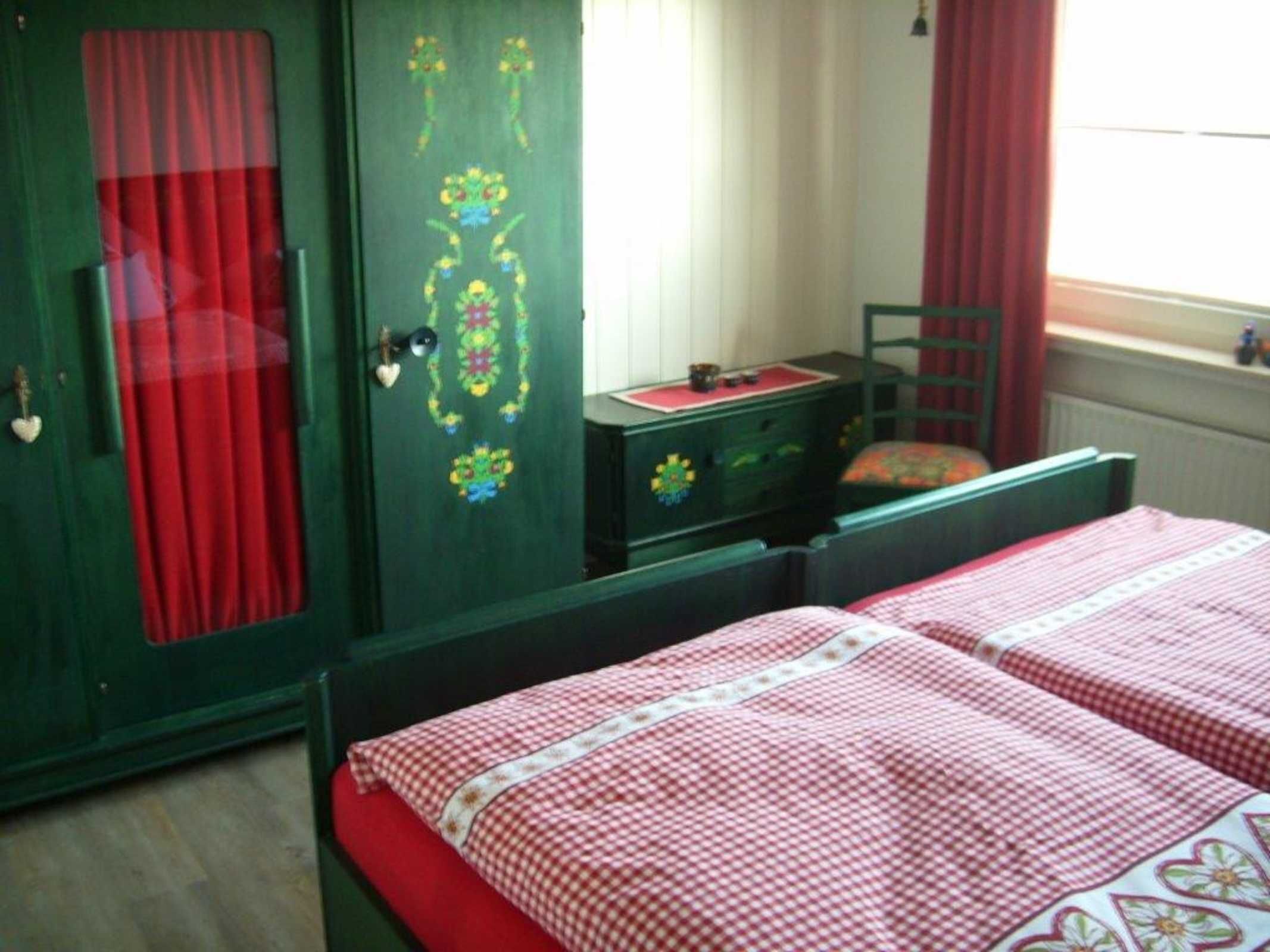 A room with two beds, a green wardrobe, and a window with red curtains.