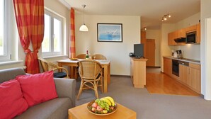 A modern living room with a sofa, dining table, and a fruit bowl. There is a kitchen area with wooden cabinets and a microwave. - Holiday home 12 - Villa Celia Sellin (Sellin)