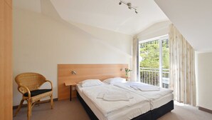 A bedroom with a large bed, a wooden headboard, a wicker chair, and a view of greenery through the window. - Holiday home 12 - Villa Celia Sellin (Sellin)