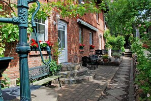 Un bâtiment en briques avec une porte d’entrée, des marches menant à un porche, un banc et des sièges extérieurs.